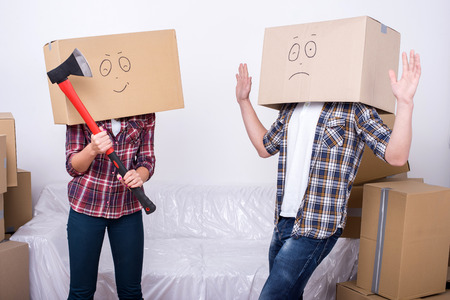 Cheerful young couple with cardboard boxes on their heads. A woman holds an ax.の写真素材