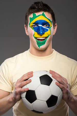 Portrait of young man with soccer ball and brazilian flag painted on his face.の写真素材
