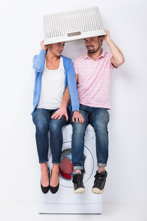 Young smiling couple with basket are sitting on the washing machine on the white .の写真素材