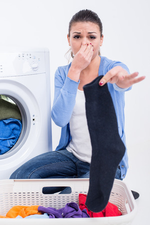 Young woman near the washing machine is keeping smelly sock.の写真素材