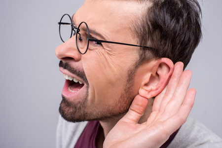 Portrait of spectacled man secretly listening on private conversation. Human face, expression, emotion, body language.の写真素材