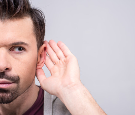 Man holds his hand to his ear.  He secretly eavesdropping on a private conversation. The human face, expression, emotion, body language.の写真素材