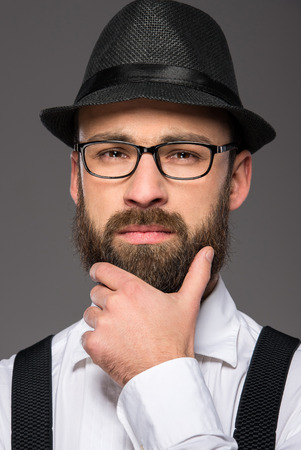 Bearded hipster man wearing hat , suspenders, a bow-tie on grey background.の写真素材
