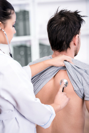 Young doctor is examining the patient lungs with a stethoscope.の写真素材