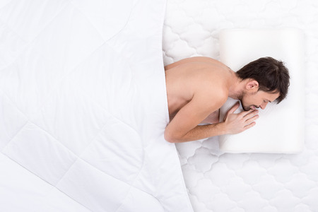A young man is sleeping on a mattress. Top view. Isolated on white backgroundの写真素材