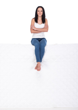 Beautiful young woman is sitting on mattress, isolated on a white background.の写真素材