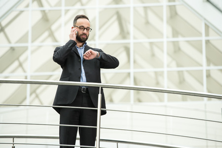 Portrait of handsome confident businessman is looking  at clock and speaking by phone.