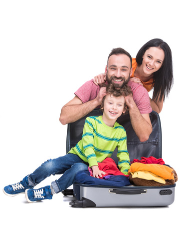Happy cheerful parents and their son in a suitcase, isolated on white background.の写真素材