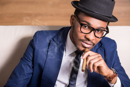 Young black man is wearing suit and hat, smoking a cigar.の写真素材