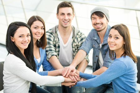 Group of young and diverse people are joining hands. Smiling and looking at the camera.