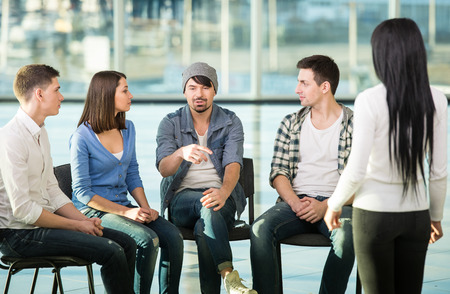 Young woman is sharing her problems with people. View of woman is telling something and gesturing while group of people are sitting in front of her and listening.の写真素材