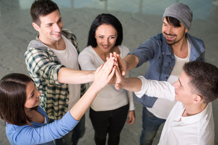 Group of cheerful young people are standing close to each other and holding hands up.の写真素材
