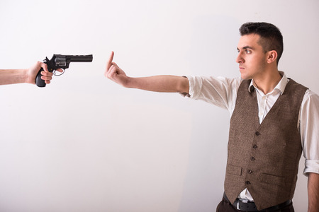 Hand is holding a gun and man with finger up. Grey background.の写真素材