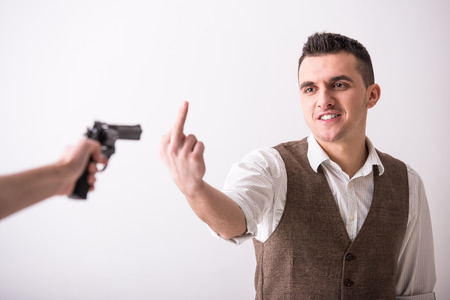 Hand is holding a gun and man with finger up. の写真素材