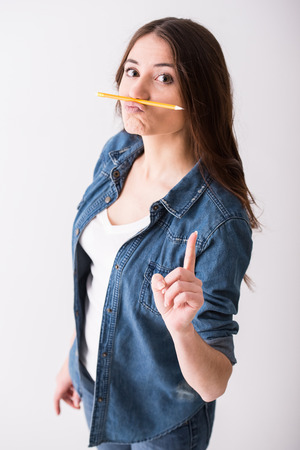 Portrait of a funny girl with pencil between nose and lips on a grey background.の写真素材