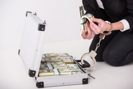 Young woman with a suitcase full of money and handcuffs. Close-up.の写真素材