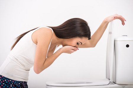 Young woman vomiting into the toilet bowl in the early stages of pregnancy or after a night of partying and drinking.の写真素材