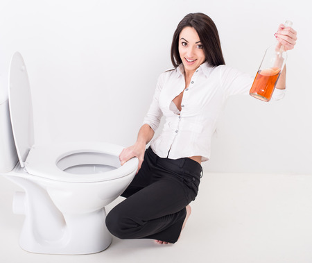 Top view of drunk woman is sitting on the toilet floor and is holding a whisky bottle.の写真素材