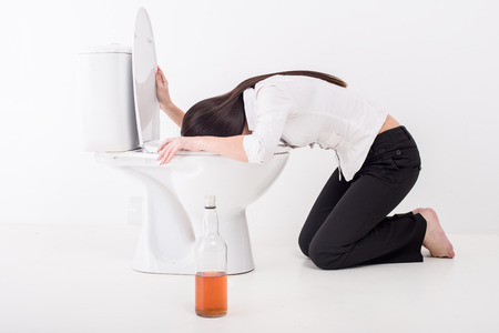 Drunk woman vomiting on a toilet bowl. Bottle with alcohol on the floor.の写真素材
