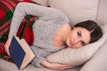 Top view of young woman is holding a book lying on sofa at home.
