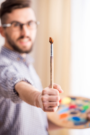 Portrait of a young male artist is holding a brush and mix color oil painting on palette.の写真素材