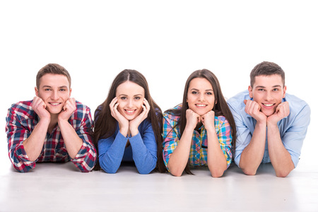 Front view of young people are lying, smiling on floor looking at camera, over white background.