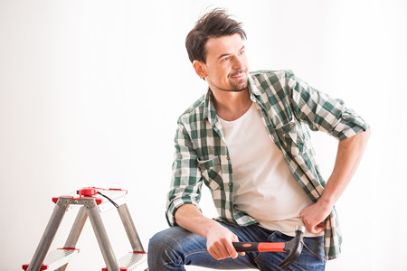 Repair home. Young man is standing with stepladder, hammer and wall on the background.の写真素材