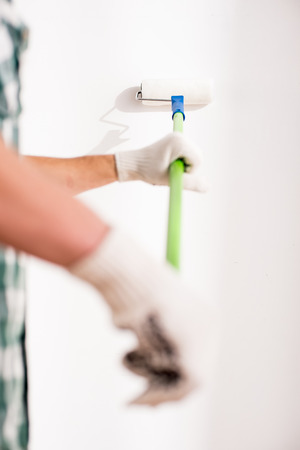 Close-up hands of young man is doing repair at home with roller for painting a wall.の写真素材
