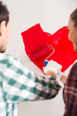 Young happy couple are painting a heart on the wall while doing repair at home.の写真素材