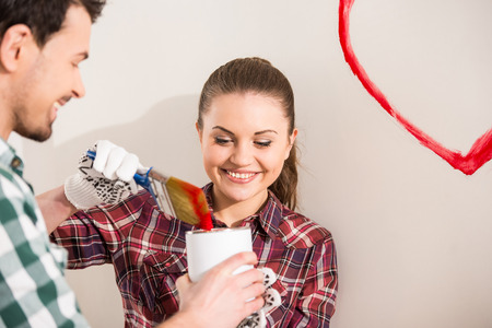 Young happy couple are painting a heart on the wall while doing repair at home.の写真素材