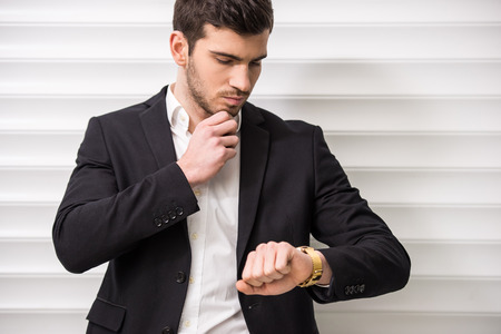 Young trendy man is posing with watch in front of a wall.