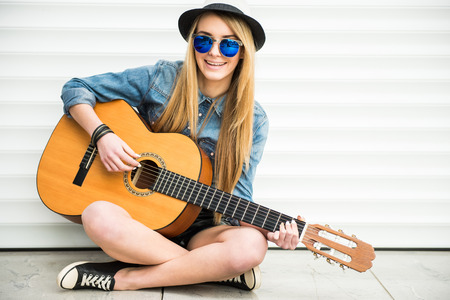 Young beautiful, trendy girl with acoustic guitar is playing sitting on the floor.