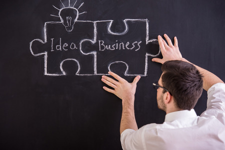 Young man is connecting puzzles chalk drawing on blackboard. Idea and business concept.の写真素材