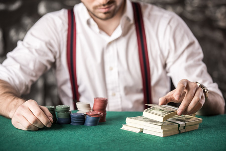 Close-up hand of young man, while playing poker game, with money and chips.
