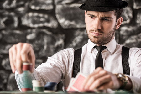 View of young, confident, gangster man in shirt, suspenders and hat, while he's playing poker game.の写真素材