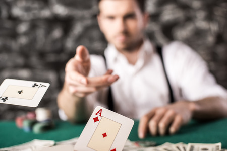 Young, confident, gangster man in shirt and suspenders, is throwing his cards on poker table, while he's playing poker game.の写真素材