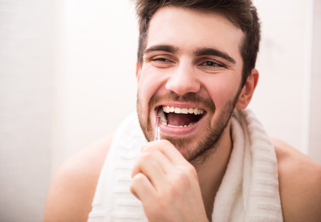 Morning routine of washing the teeth. Handsome young man is brushing teeth with toothbrush and smiling.の写真素材