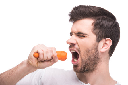 Side view of young man is eating a carrot, isolated over white background. Healthy eating.の写真素材
