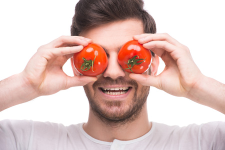 Handsome young man is holding tomatoes in front of his eyes while standing against white background.の写真素材