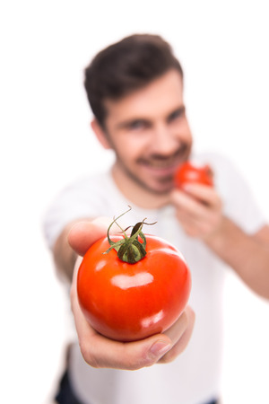 Handsome young man is holding a tomatoes, standing against white background.の写真素材