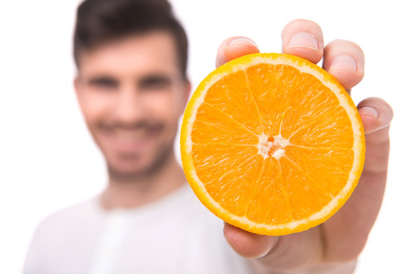 Handsome young man is holding an orange, standing against white background.の写真素材
