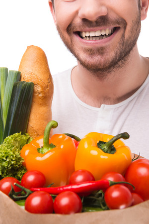 Young man is holding a bag full of vegetables, on white background.の写真素材