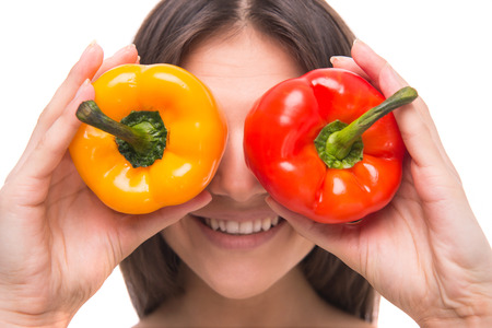 Handsome young woman is holding salad peppers in front of her eyes while standing against white background.の写真素材