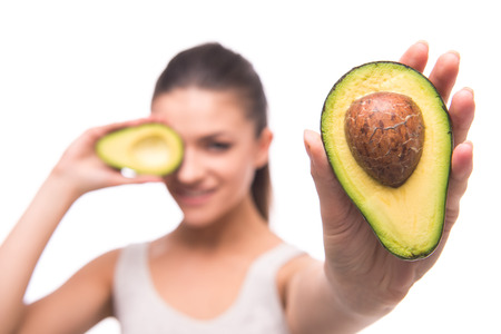 Young, smiling woman is holding avocado in front of her eyes on white background.の写真素材