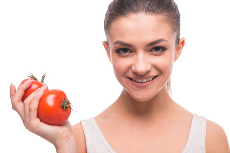 Smiling young woman is holding tomatoes, while standing against white background.の写真素材