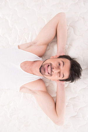 Young man is lying on the quality mattress and looking at the camera, over white backgroundの写真素材