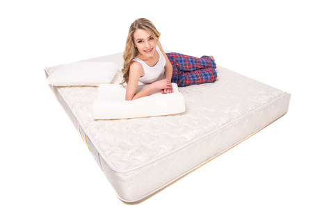 Young, smiling woman is lying on the quality mattress and looking at the camra, over white background.の写真素材