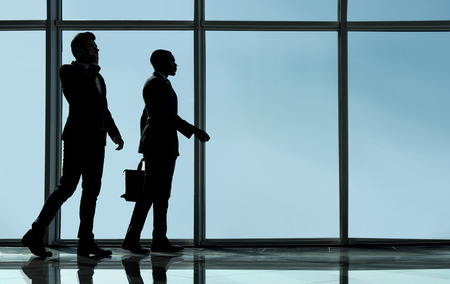 Silhouette view of two young businessmen are standing in modern office with panoramic windows.の写真素材