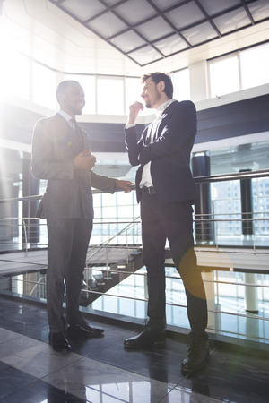 Two young businessmen are talking while standing at modern office.の写真素材