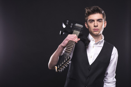 Young guitarist with the electric guitar, isolated on dark background is looking at the camera.の写真素材